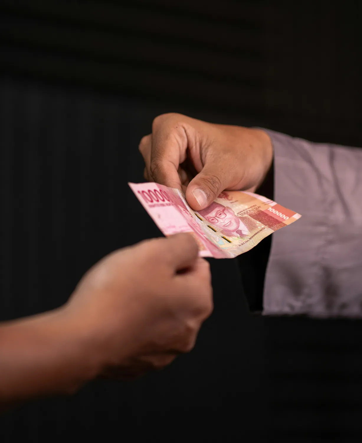 Hands exchanging Indonesian rupiah banknotes