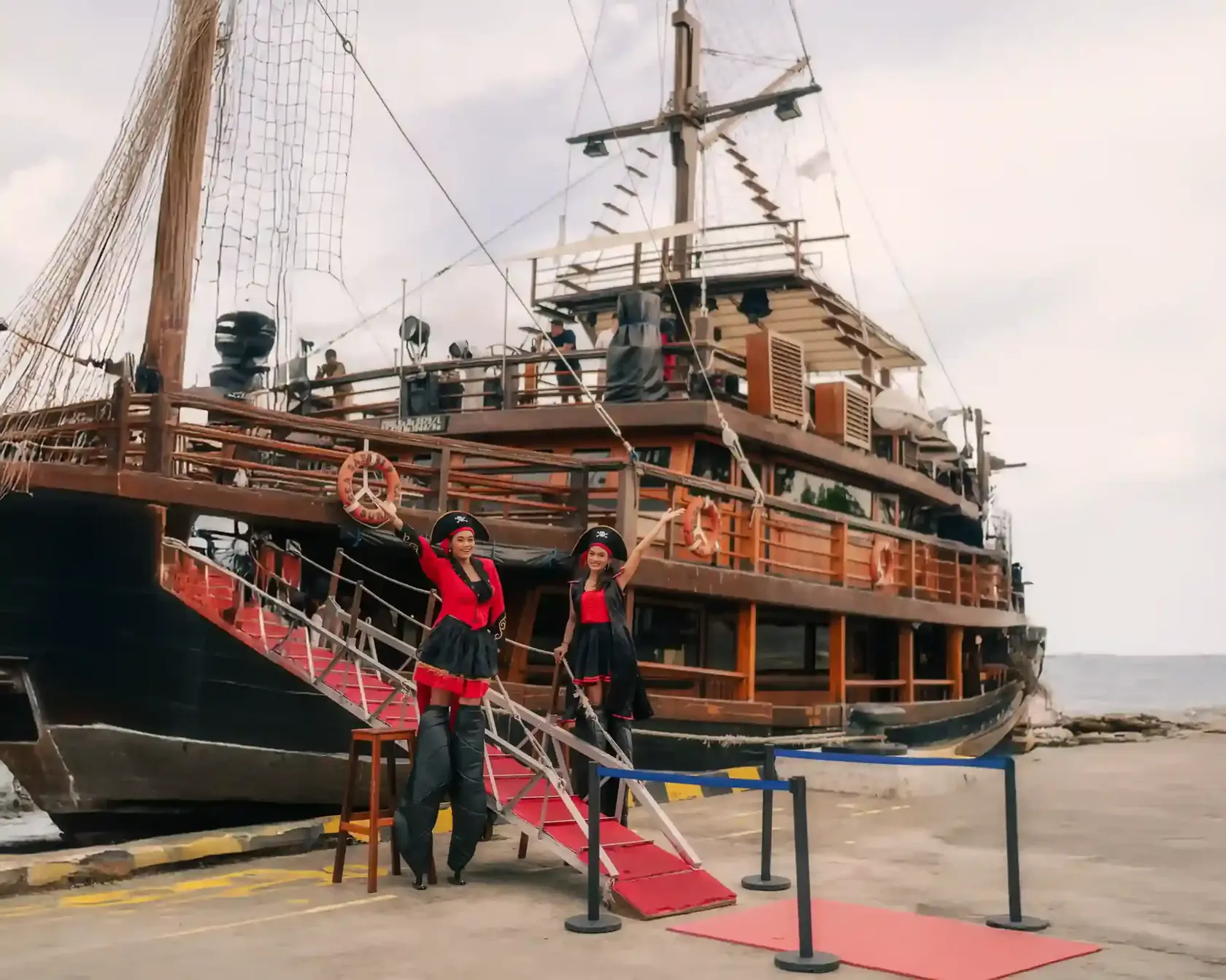 Traditional pirate-style cruise ship docked, with the crew waving from the deck